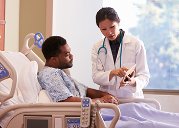 Patient in hospital bed reviews his test results with the doctor on the doctor's tablet